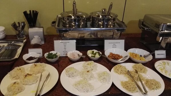 A buffet setup with various dishes including rice, noodles, and sauces.