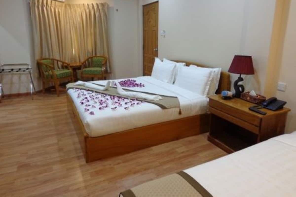 Una camera d'albergo ordinata con un letto di legno, un comodino con una lampada e due sedie.