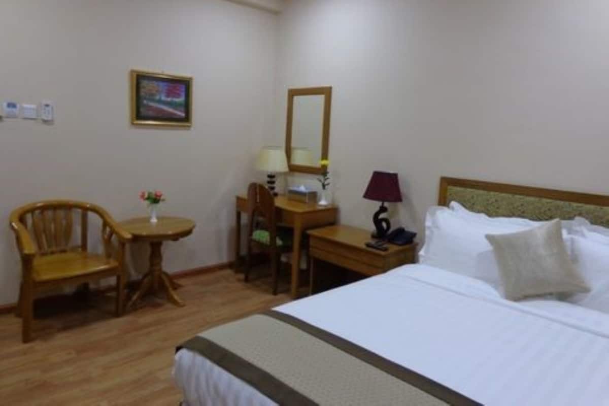 Una camera d'albergo con un letto, una scrivania, due sedie, un tavolino con un vaso, una lampada e uno specchio.