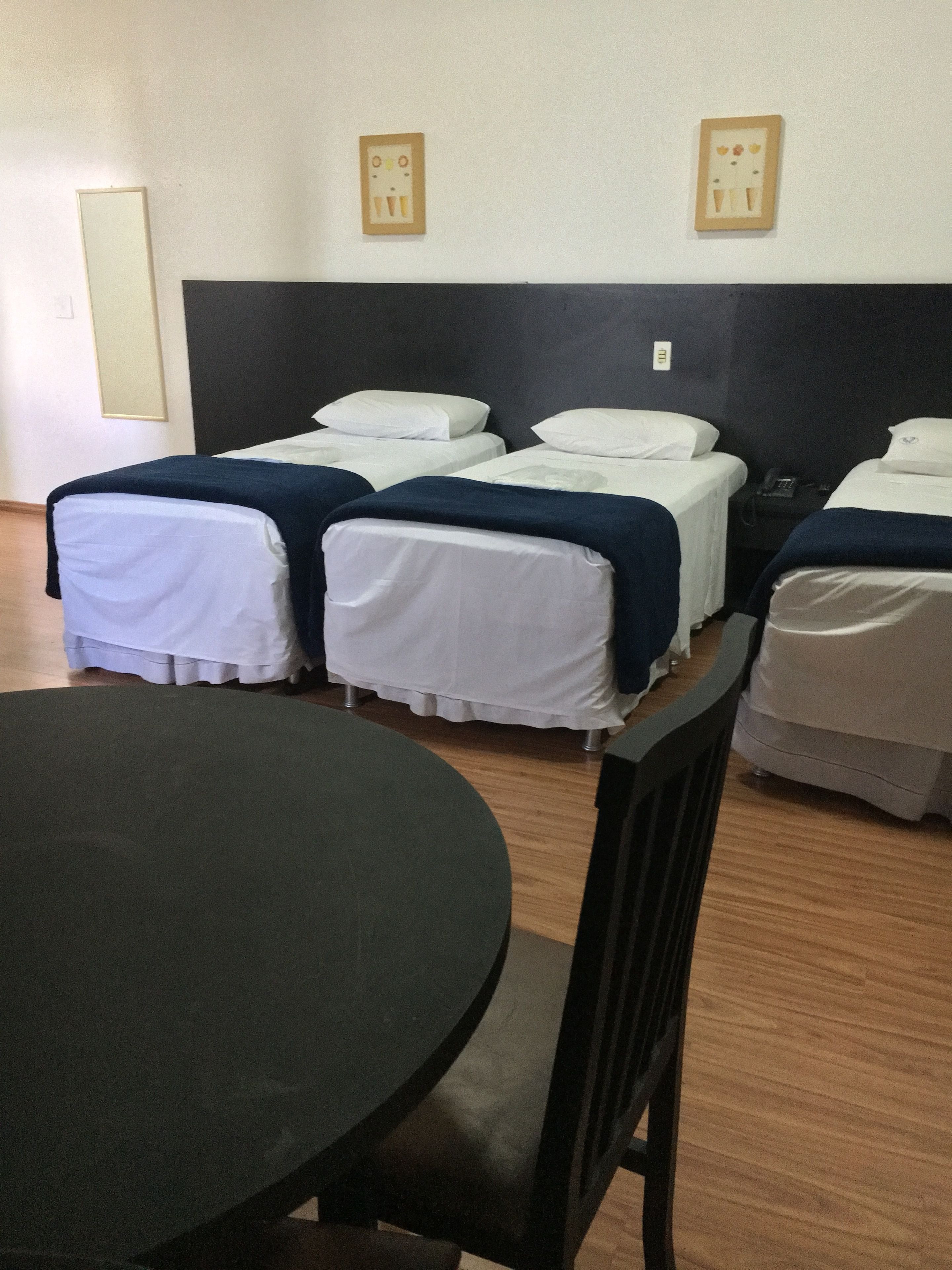 A hotel room with four single beds, a round table, and a dark-colored headboard.