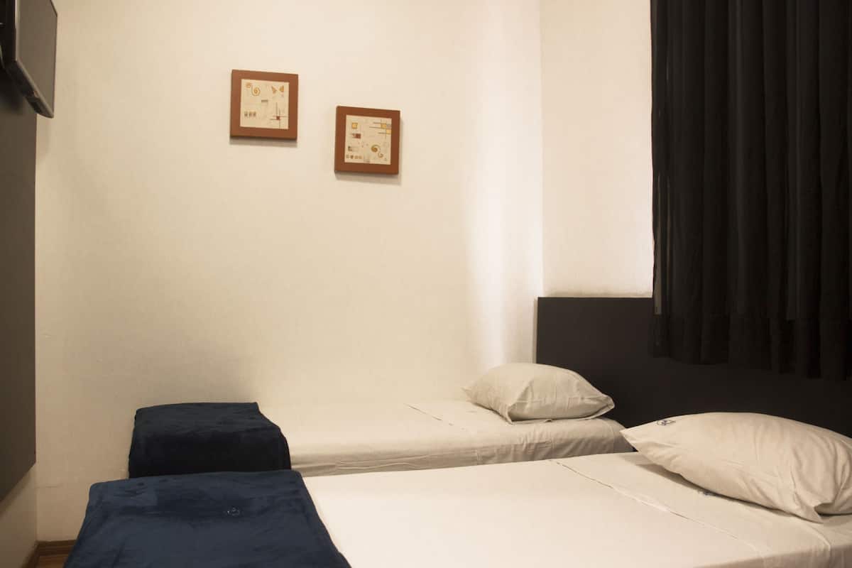 Una habitación pequeña y sencilla con dos camas, una mesita y dos cuadros en la pared.