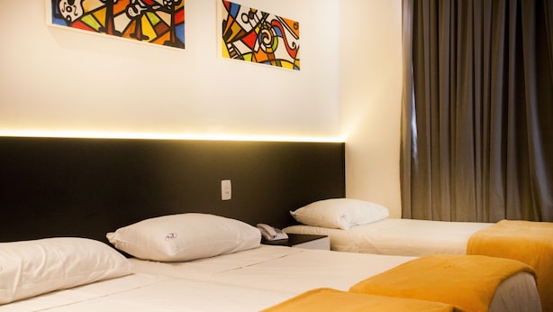 Habitación de hotel con dos camas, ropa de cama blanca, cabecero negro, un teléfono y dos cuadros abstractos de colores en la pared.