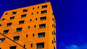 Un edificio alto anaranjado con muchas ventanas y un cielo azul despejado.