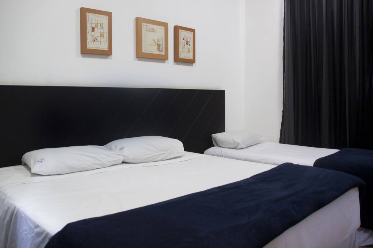 Una habitación de hotel con dos camas, un cabecero negro y dos cuadros en la pared.