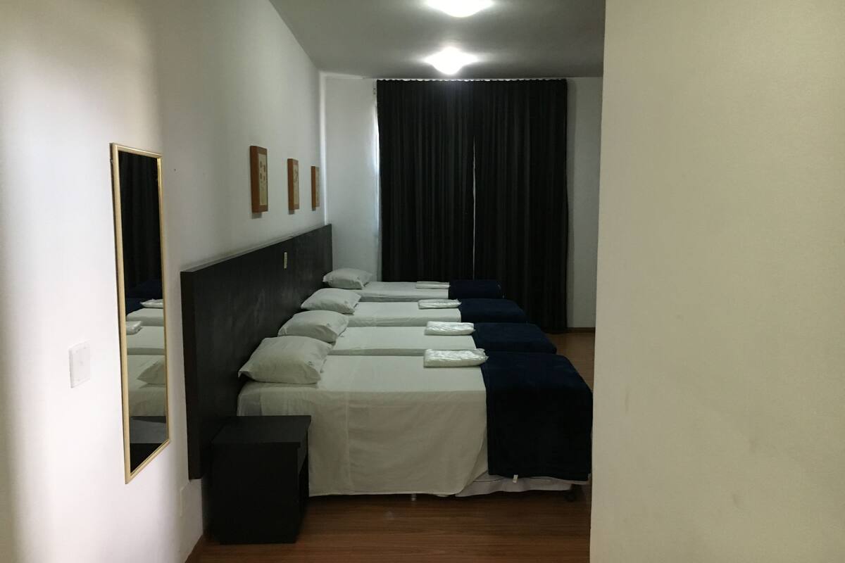 Una habitación de hotel con varias camas, un espejo y una cortina oscura.