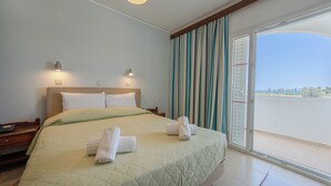 A hotel room with a large bed, two bedside lamps, a nightstand, and a view through a sliding glass door. - Tropical Sol (Kos)