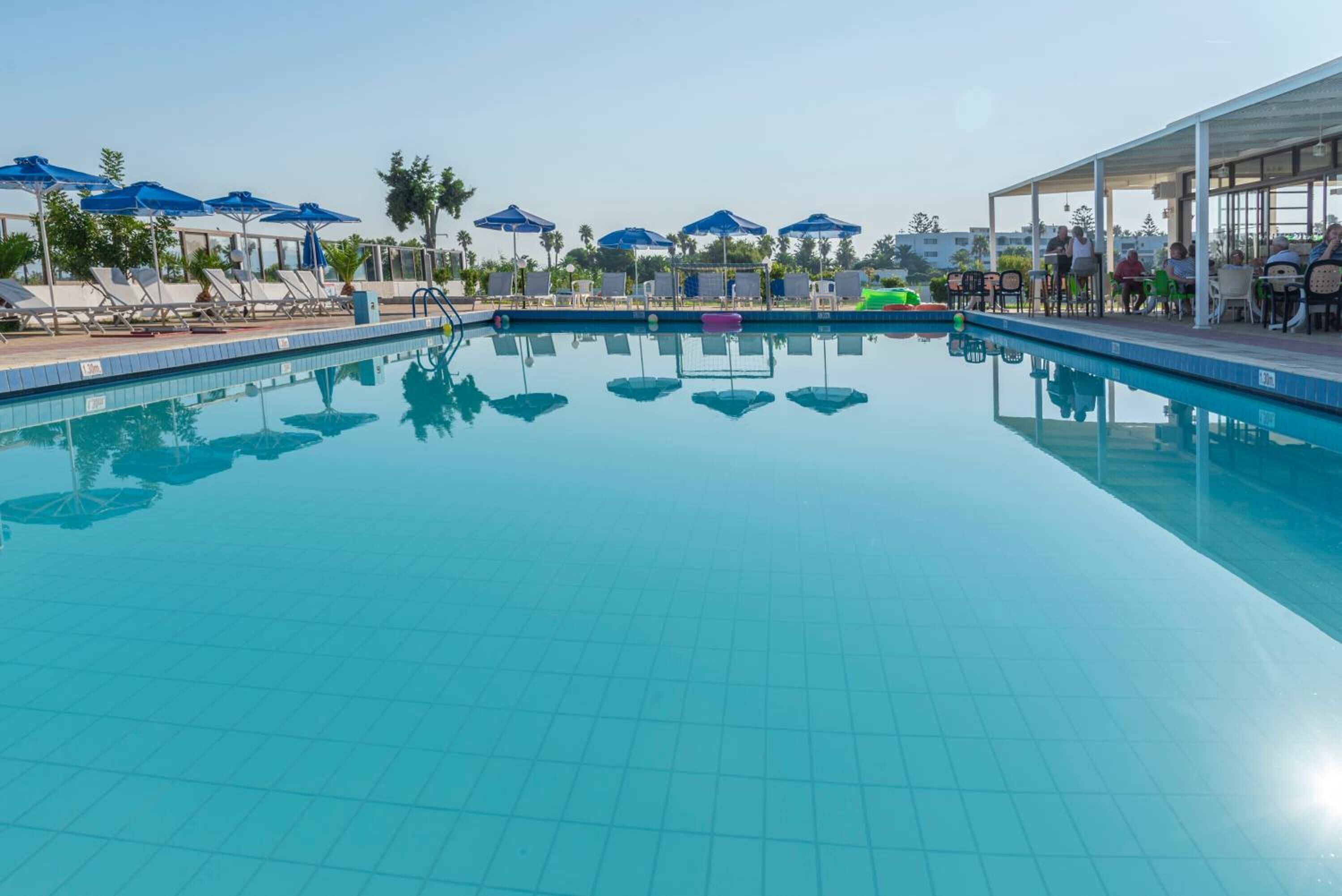 A clear blue swimming pool with lounge chairs and umbrellas, surrounded by a covered seating area.