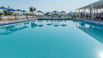 A clear blue swimming pool with lounge chairs and umbrellas, surrounded by a covered seating area.