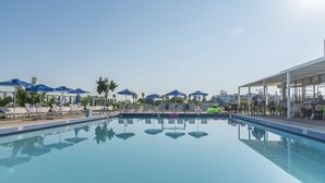 A swimming pool with lounge chairs and umbrellas, surrounded by a covered seating area. - Tropical Sol (Kos)