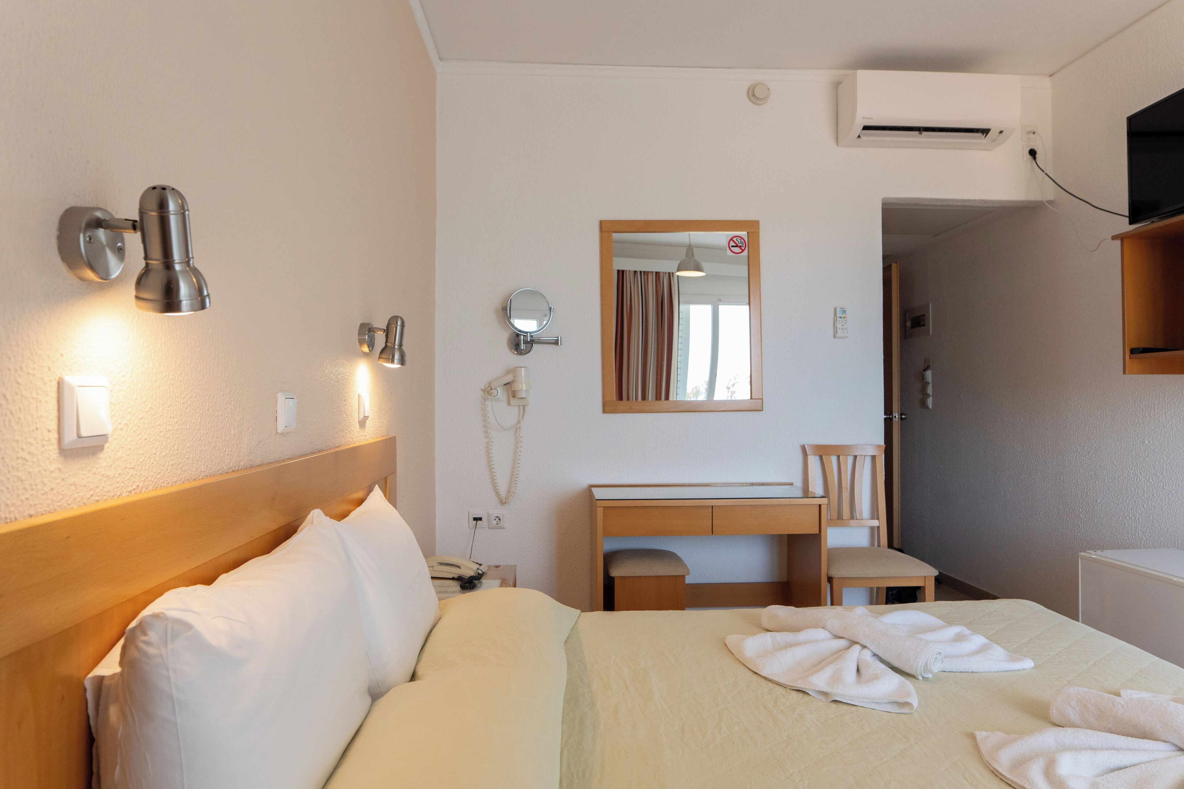Una habitación de hotel con cama, mesita de noche, escritorio, silla y espejo.