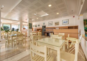 A spacious dining area with multiple tables and chairs, a kitchen area with a stove and refrigerator, and framed artwork on the walls.