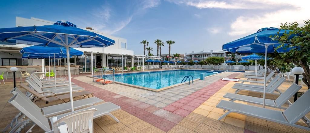 A pool area with lounge chairs and umbrellas, a clear sky, and palm trees in the background.