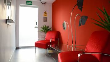 A reception area with red chairs, a glass table, a potted plant, and a wall with emergency exit signs.