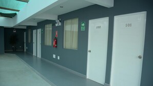 A hallway with doors numbered 101, 102, and 103, a fire extinguisher, and a green exit sign. - Hostal Villa Santa (La Victoria)