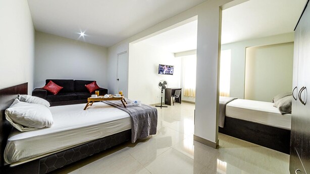 A modern hotel room with a large bed, a sofa, a desk, and a TV. - Hostal Villa Santa (La Victoria)