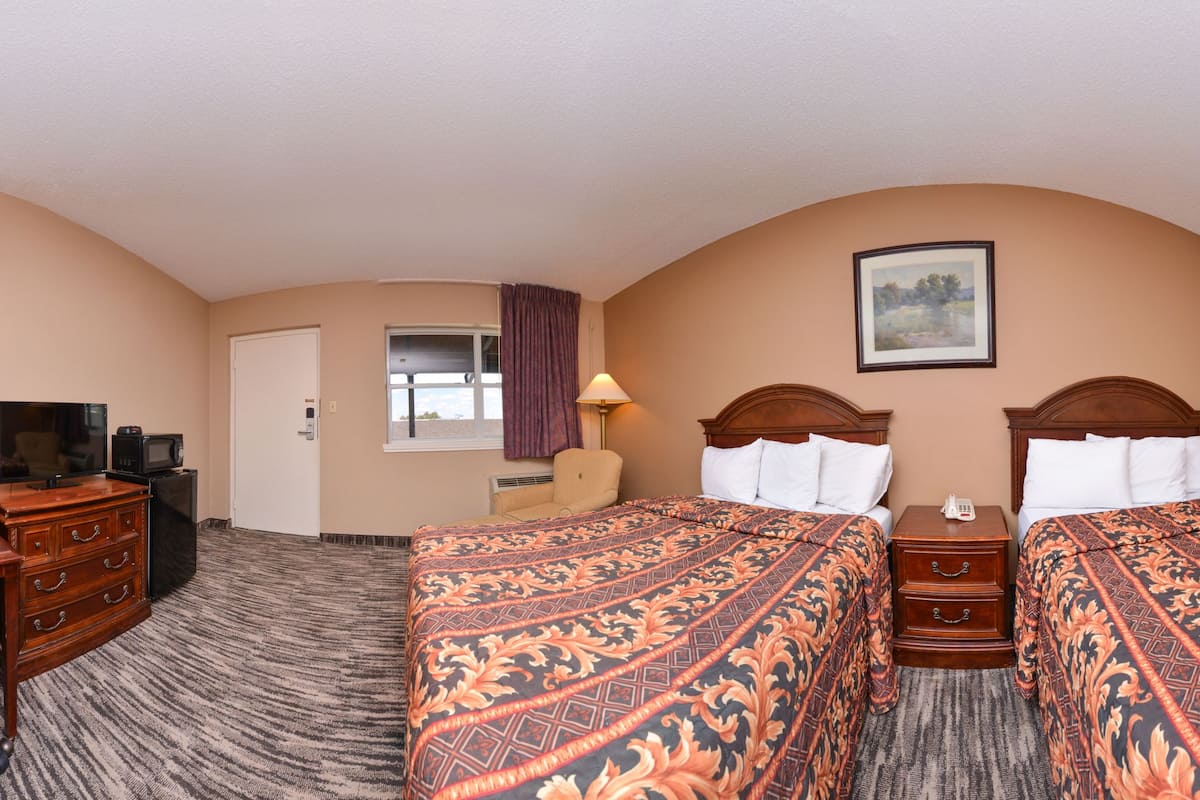 A hotel room with two beds, a desk, a chair, a TV, and a telephone.