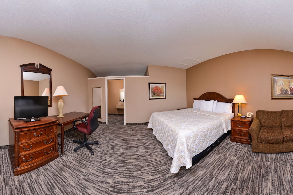 A hotel room with a bed, a desk with a computer, a chair, a couch, a lamp, and a television.