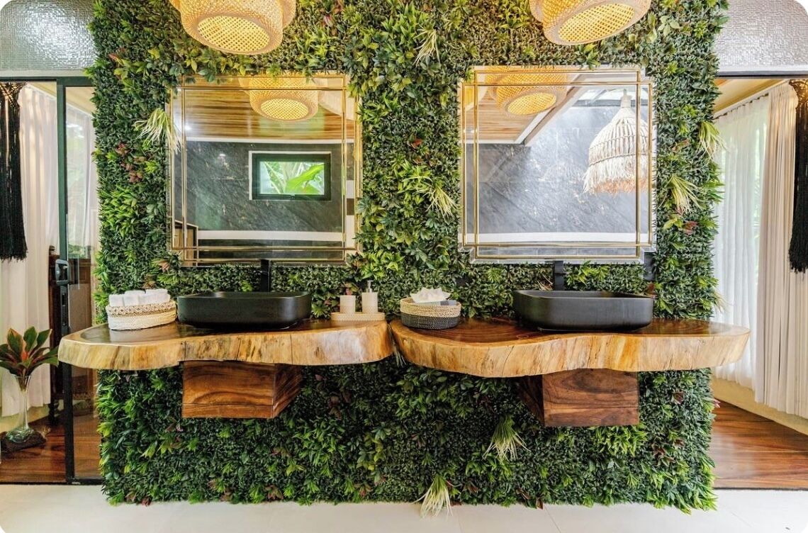 A bathroom with two sinks, each with a mirror and a black basin, set against a wall covered with green foliage.