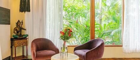 A room with two purple chairs, a small round table, a statue, and a window with a view of greenery.