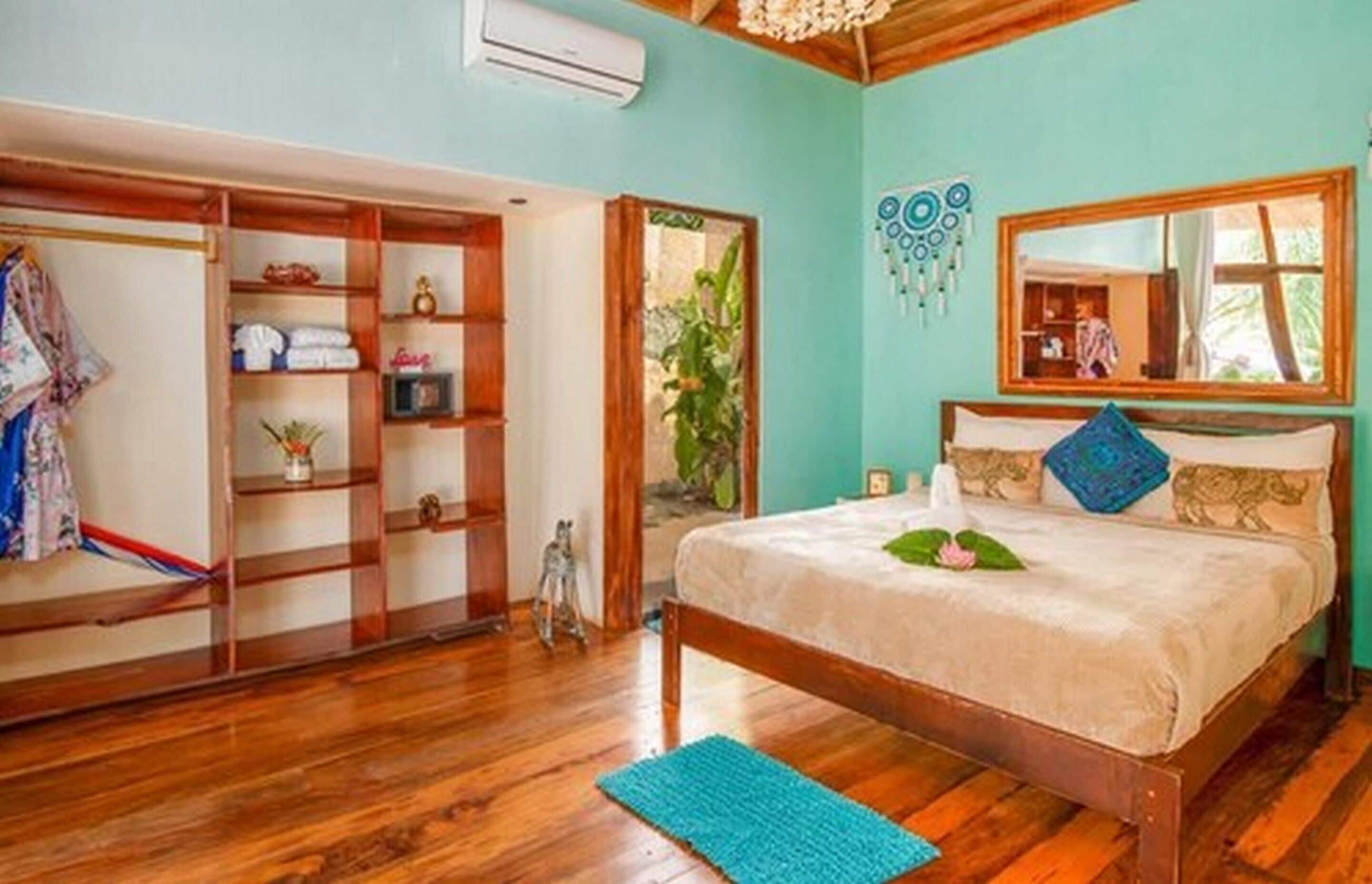 Ein Schlafzimmer mit einem hölzernen Bett, einem Kleiderschrank, einem Spiegel und einer kleinen Pflanze.