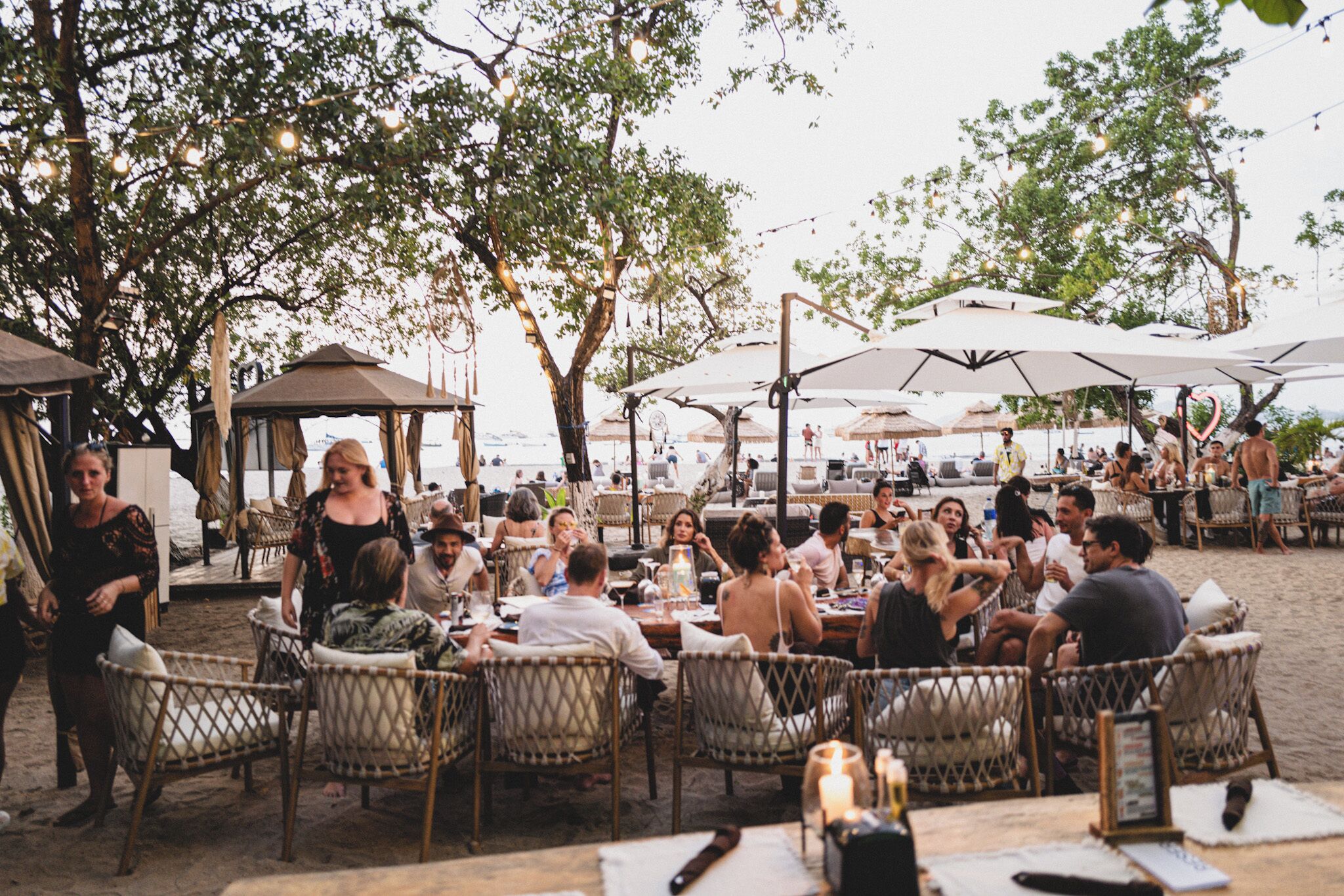 An outdoor dining area with wicker chairs and umbrellas, overlooking a beach.
