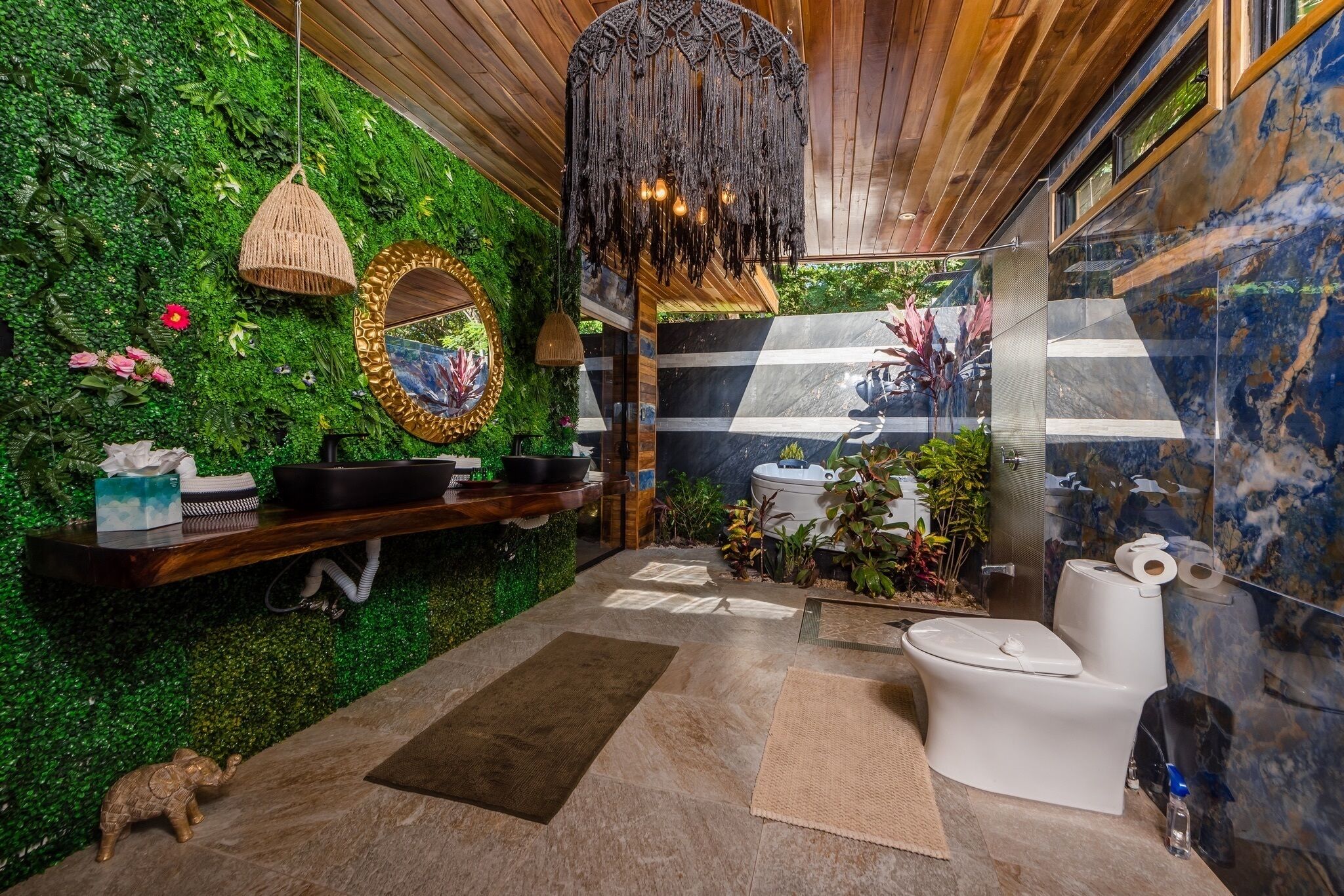 A bathroom with a green wall, a wooden vanity, a hanging light fixture, and a toilet with a marble backsplash.