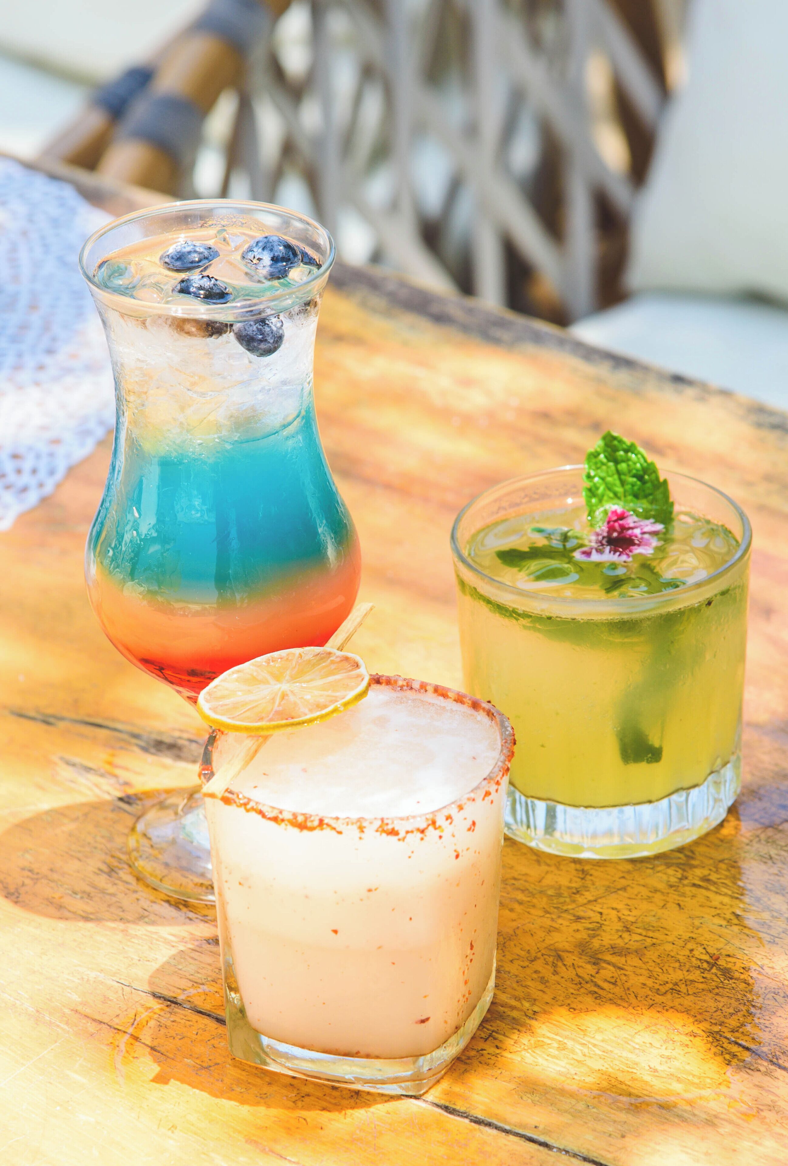 Tres bebidas sobre una mesa de madera con mantel de encaje.