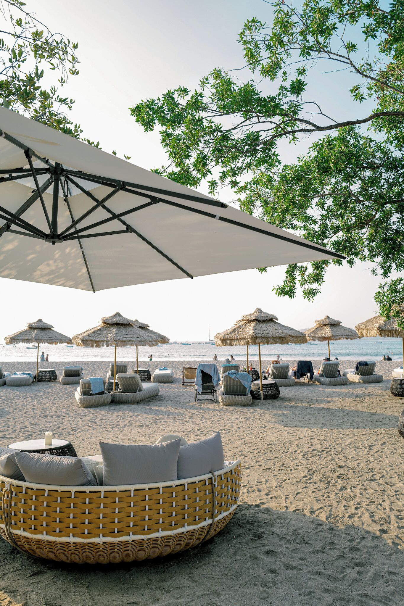 Een strandsetting met rieten ligstoelen, rieten parasols en uitzicht op zee.