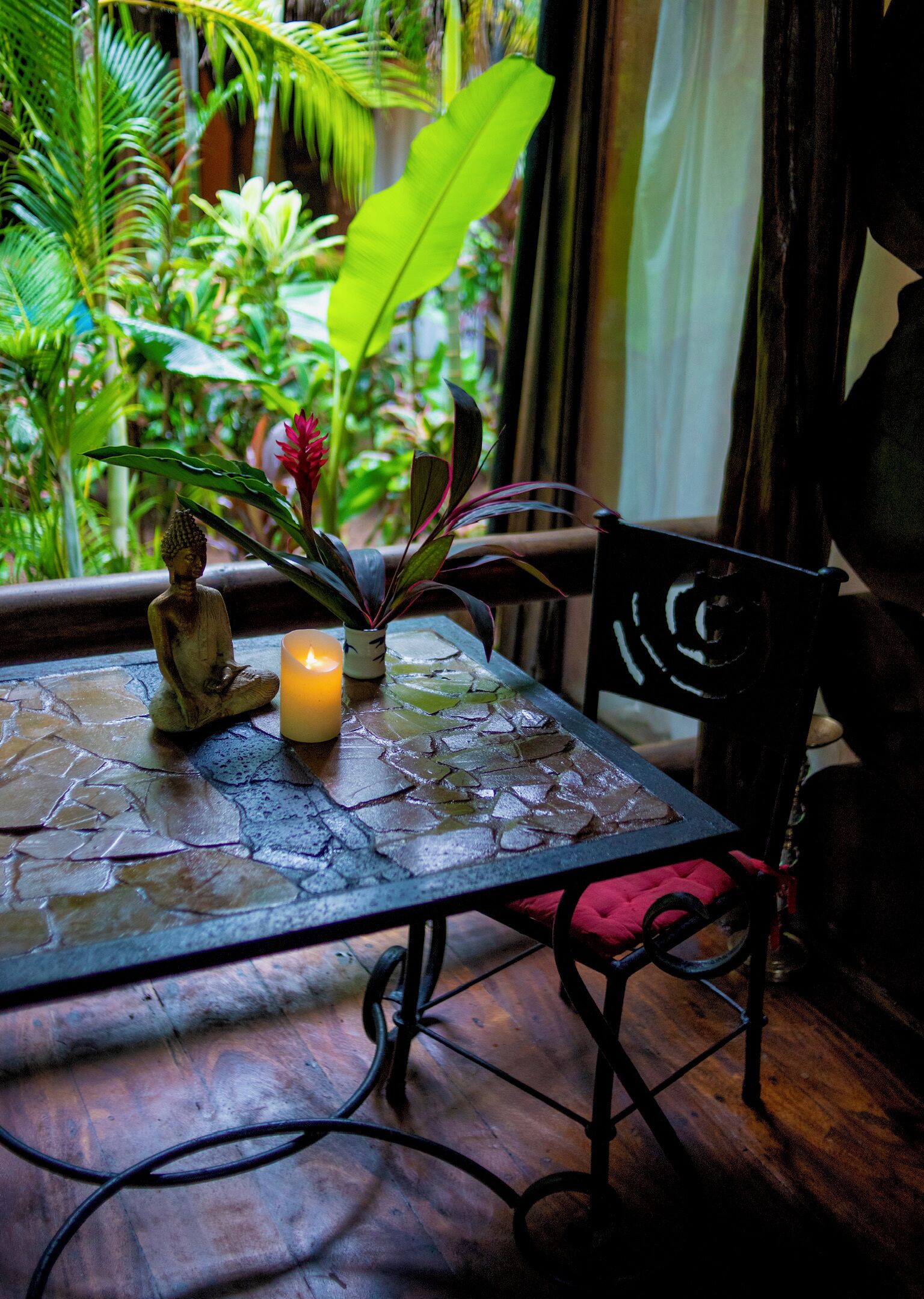 Une table ornée d’une statue de Bouddha, d’une bougie et d’une plante en pot aux fleurs rouges.