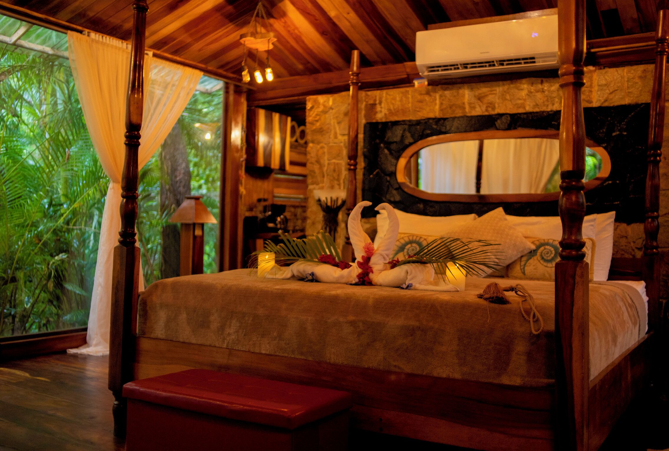 A bed with a wooden frame, a stone wall, and a large window with curtains.
