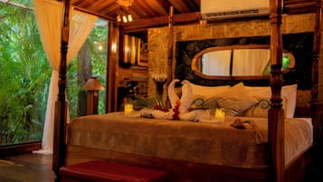 A bed with a wooden frame, a stone wall, and a large window with curtains.
