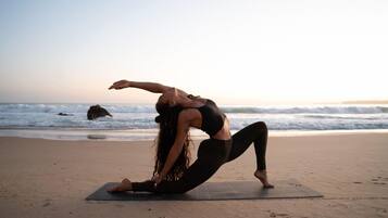 Una persona practicando yoga sobre una esterilla en la playa, con el océano de fondo.
