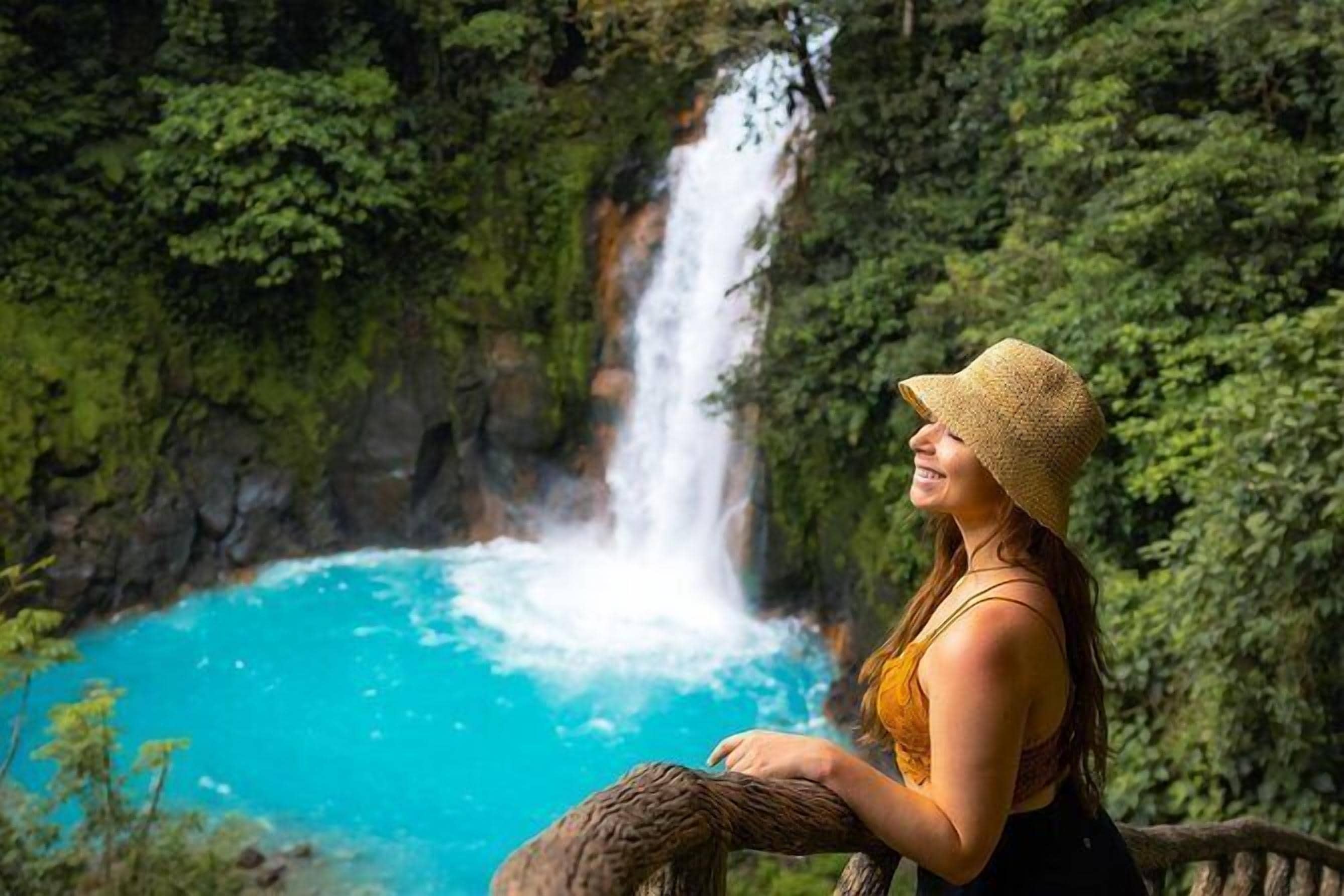 A person sitting on a tree branch overlooking a waterfall and a turquoise pool.