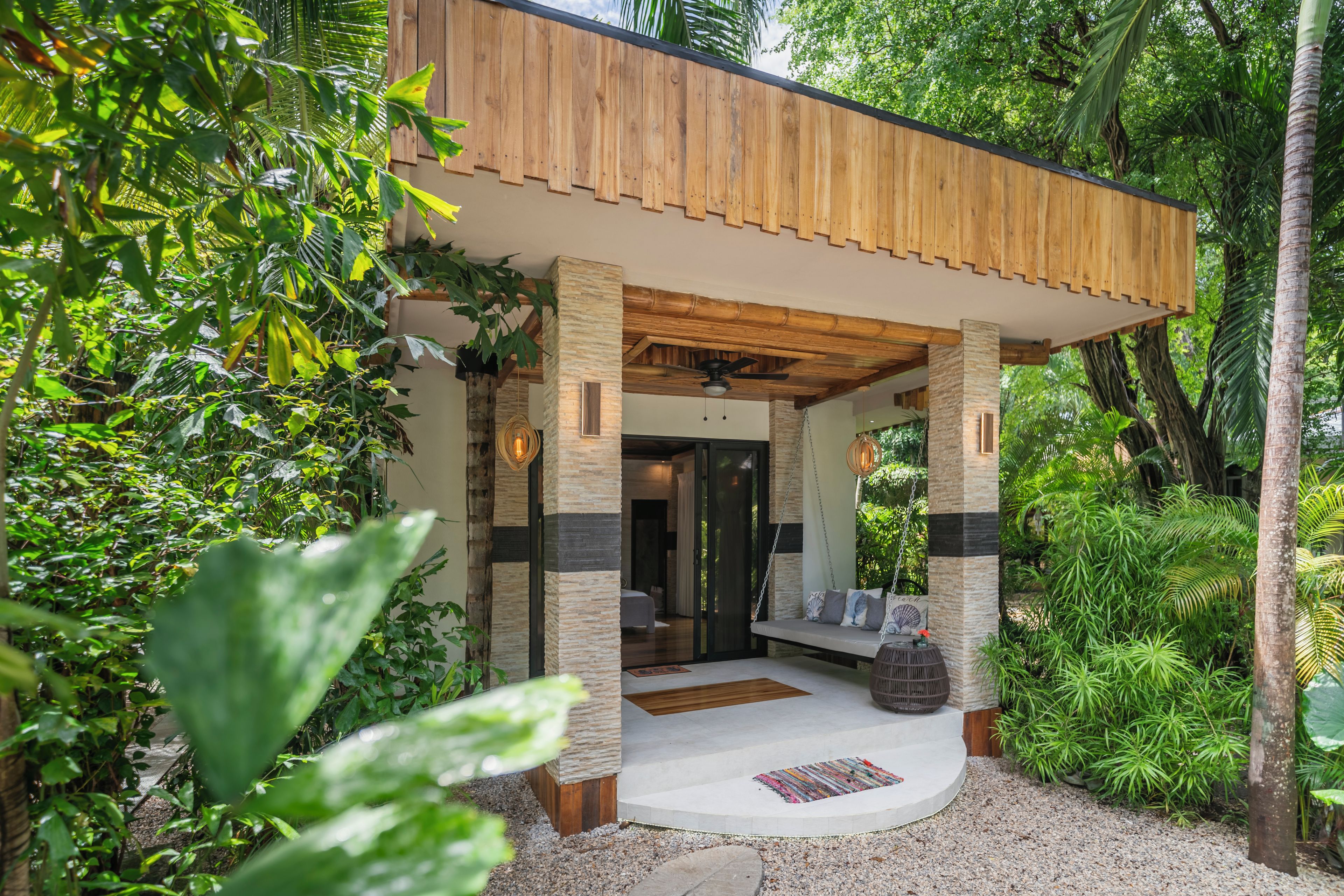 Une maison moderne dotée d’un porche en bois, de piliers en pierre et d’une balançoire.