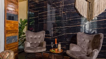 Una habitación moderna con dos sillones tapizados grises, una mesita redonda con una botella y copas, y un colgador de macramé en la pared.