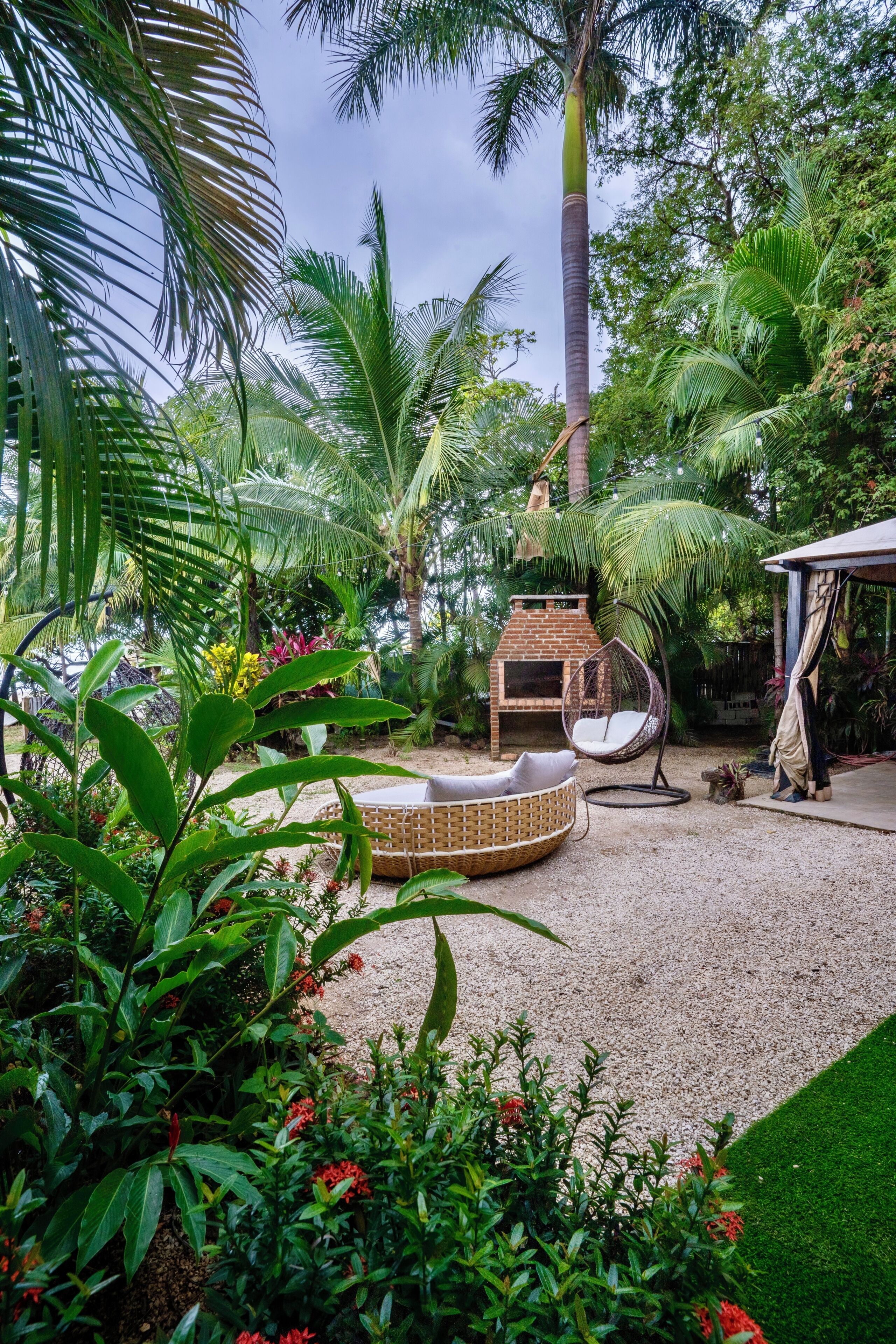 Un jardin avec un barbecue en briques, un fauteuil suspendu et un espace abrité.