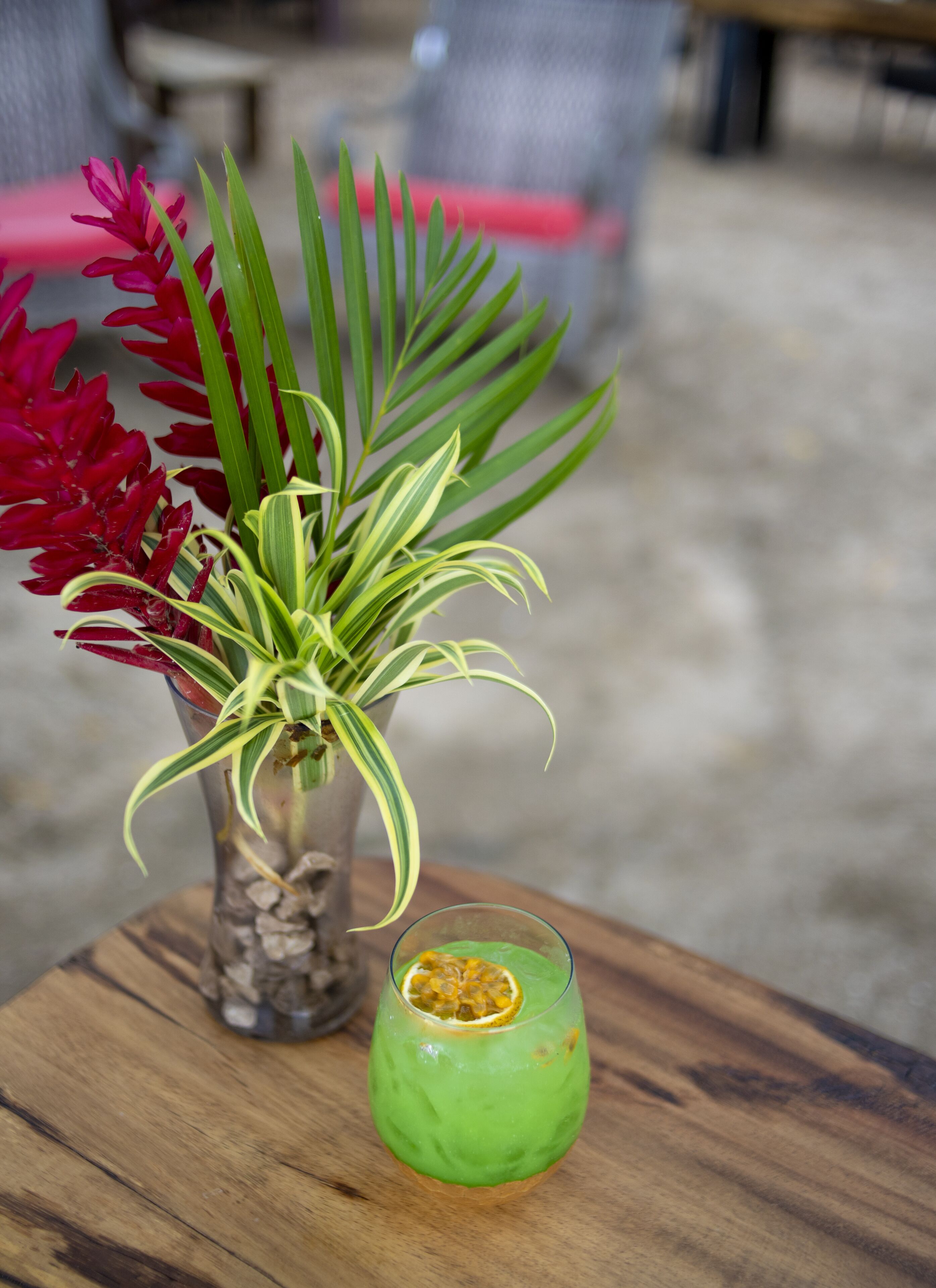 A table with a glass of green drink and a plant with red flowers and green leaves.