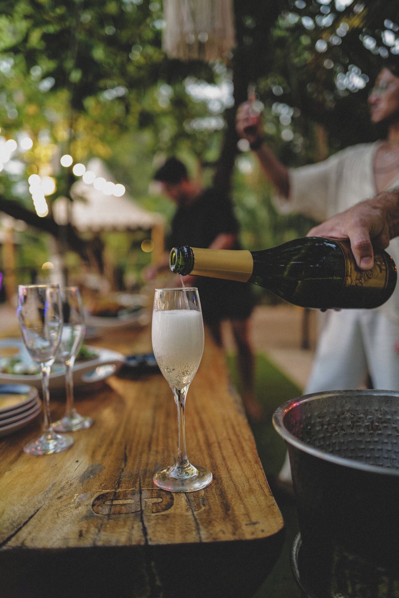 A bottle of champagne being poured into a glass on a wooden table.