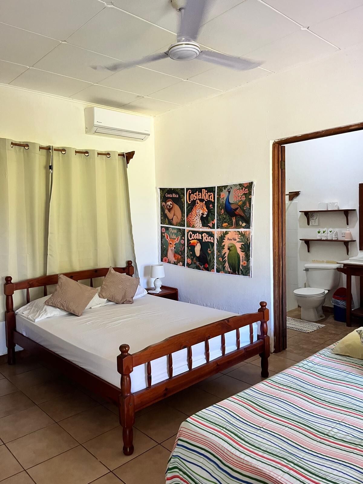 A bedroom with a wooden bed, a ceiling fan, a wall-mounted air conditioner, and a poster of Costa Rica wildlife.