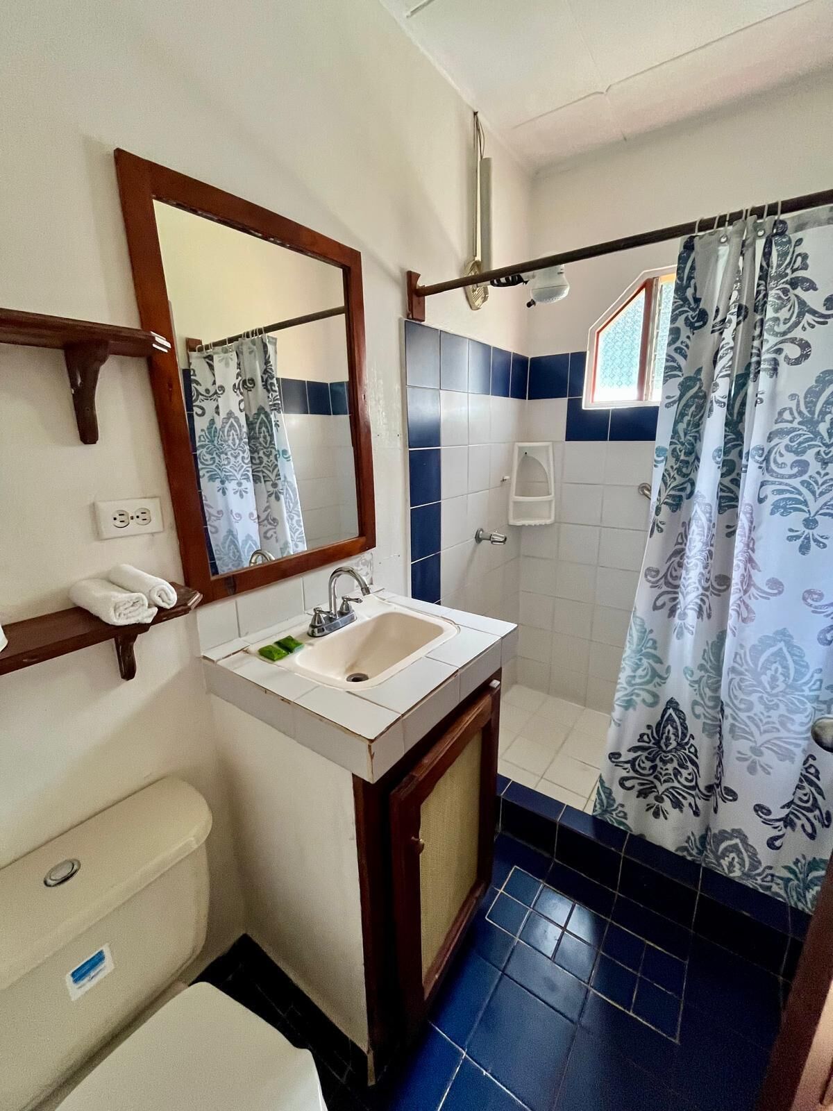 Ein Badezimmer mit weißem Waschbecken, einem Spiegel, einer Toilette und einer Duschkabine mit gemusterten Vorhängen.