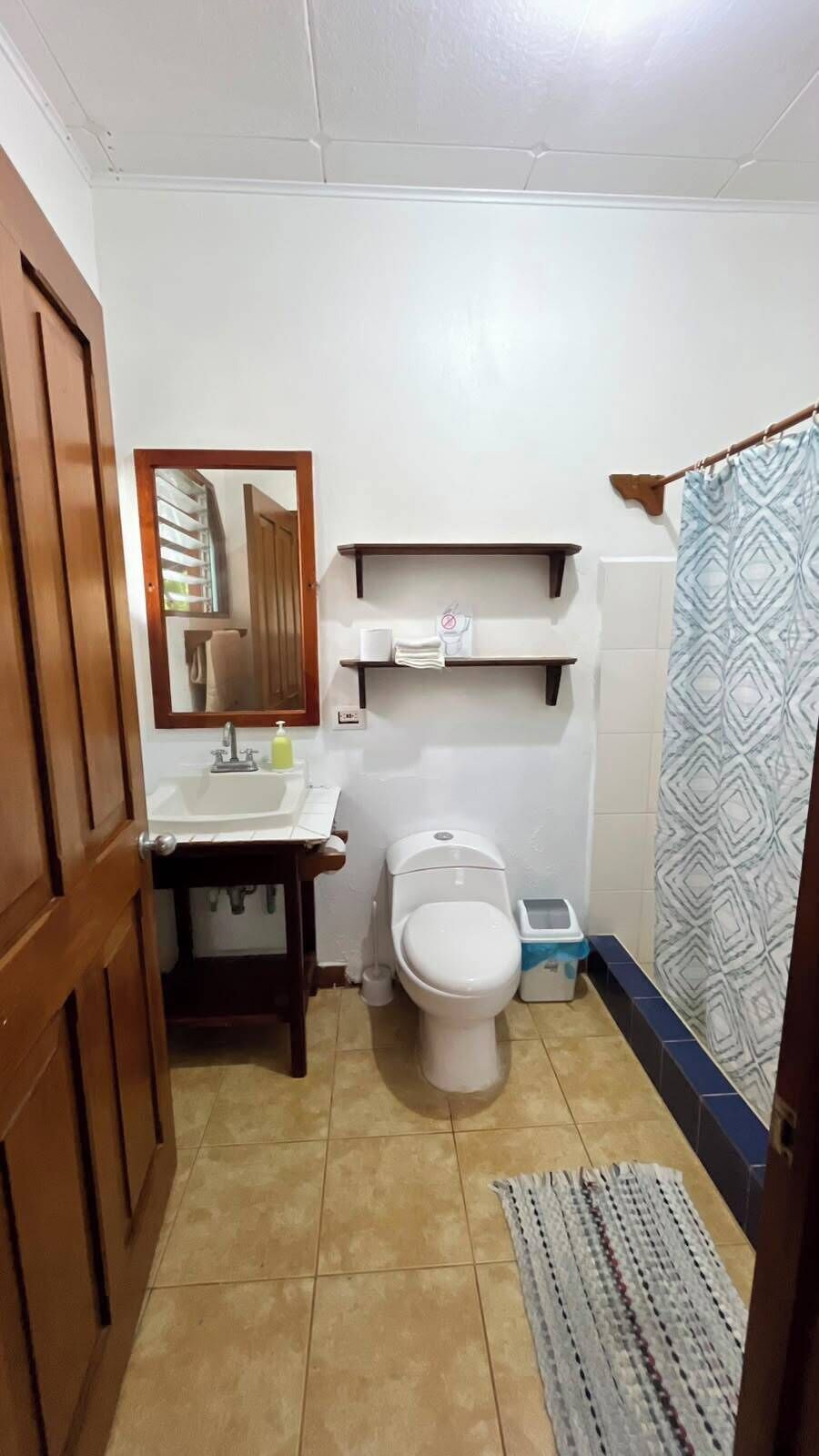 Un baño con inodoro, lavamanos, espejo y cortina de ducha.