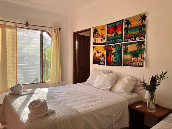 A hotel room with a bed, a nightstand, a vase with flowers, and a window with curtains.