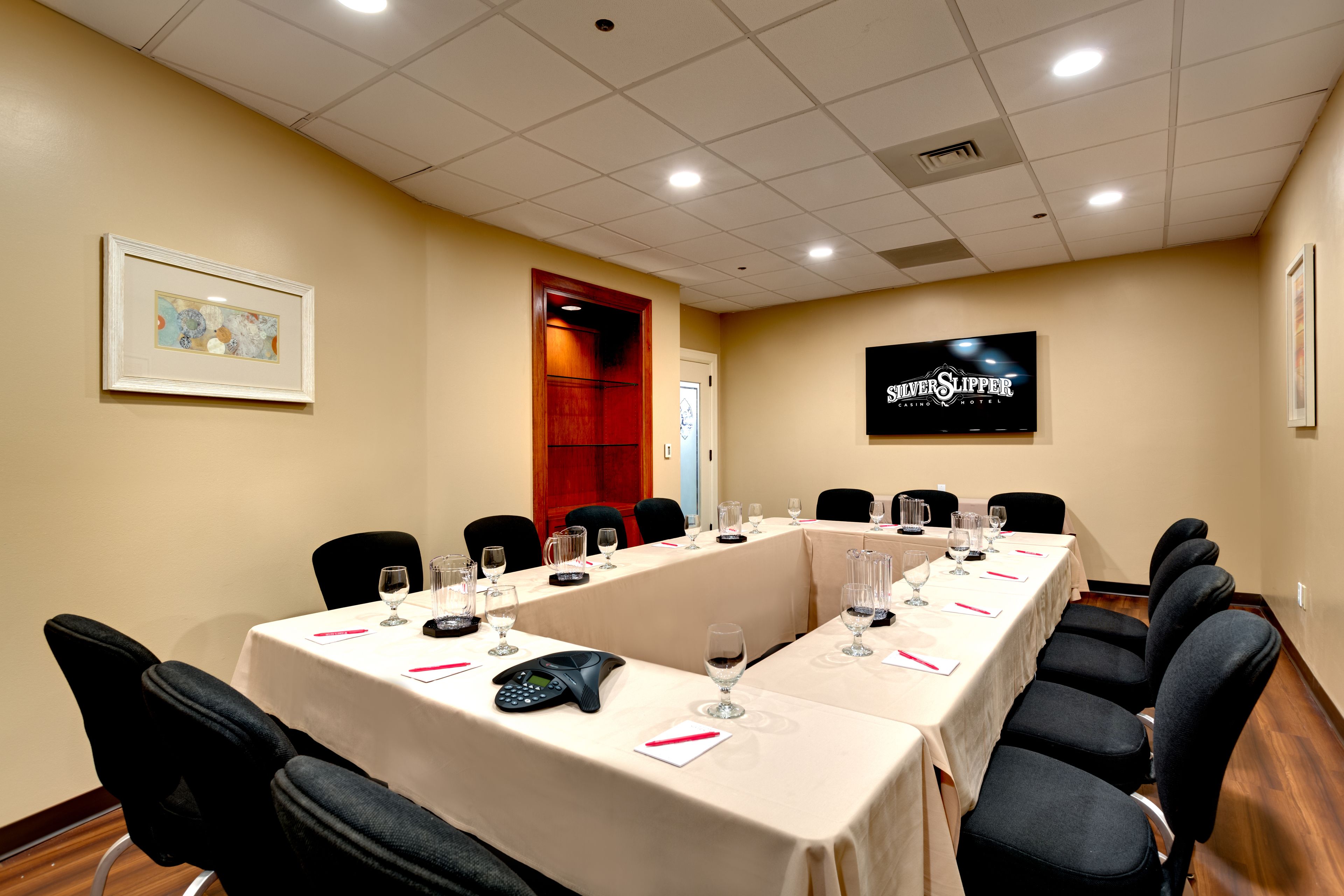 A conference room with a long table, chairs, a phone, and wine glasses.