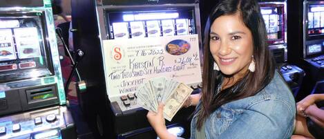 A woman holding a large check and a stack of cash in front of slot machines.