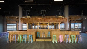 Zona de bar con techo de paja, taburetes de madera y vistas al mar a través de amplios ventanales.