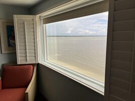 Una habitación con ventana que da a una masa de agua, una silla roja y un cuadro en la pared.