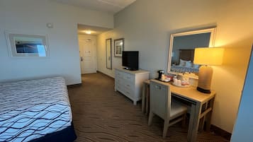 Una habitación de hotel con cama, escritorio, silla, televisor, espejo y lámpara.