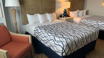 A hotel room with two beds, a nightstand, a lamp, and a chair.