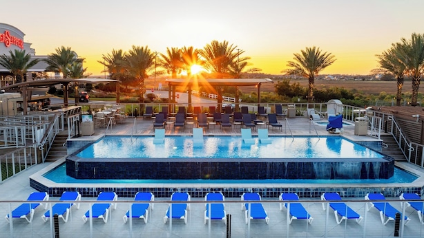 Una piscina de hotel con sillas de tomar el sol, un elemento acuático y vistas al atardecer.
