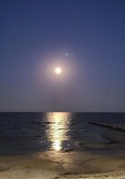 Escena de playa con un mar tranquilo y el reflejo de la luna visible en el agua.